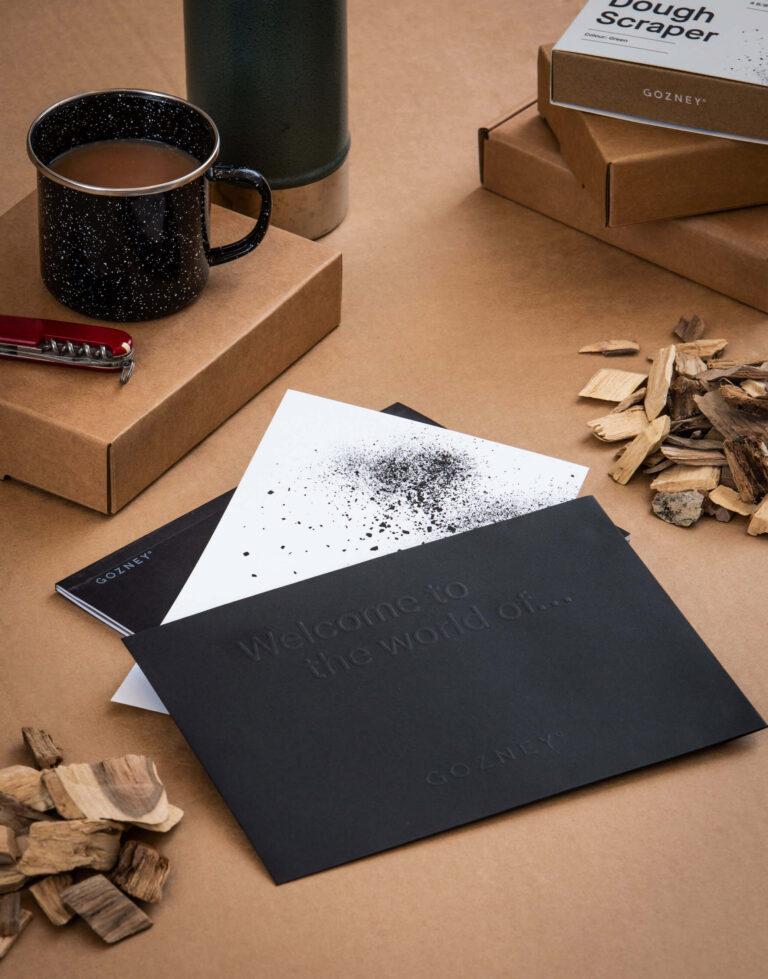 A Gozney welcome card in a black envelope arranged amongst a selection of accessories and their packaging