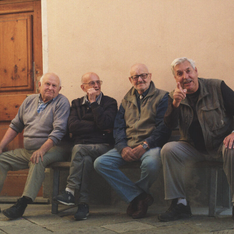 A group of older men sit on a bench together