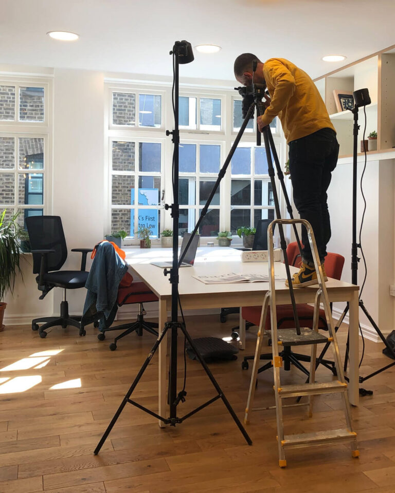 A photographer takes a shot from a camera tripod has been mounted on a white desk for a photoshoot