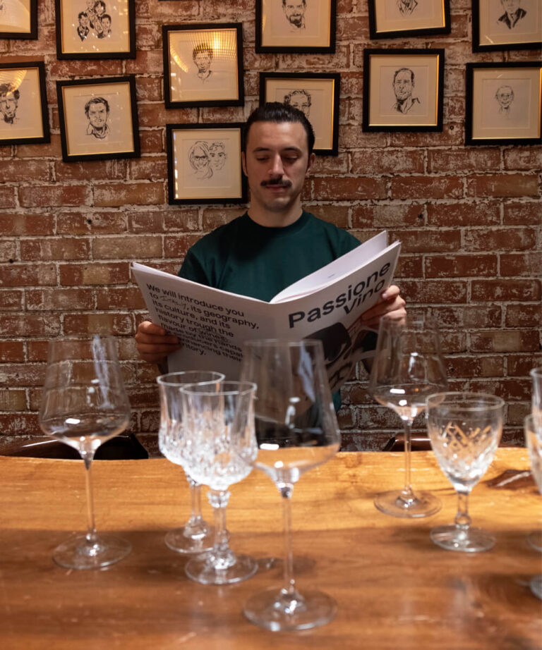 A man reads the Passione Vino newspaper at a table set with crystal glassware
